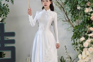 Cô dâu mặc áo dài trắng cầm ô đứng giữa không gian ngập tràn hoa trắng tinh khôi.