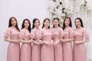 Nhóm các cô gái mặc áo dài hồng pastel chụp tại studio với hoa trắng.