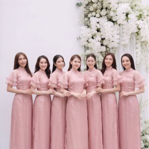 Nhóm các cô gái mặc áo dài hồng pastel chụp tại studio với hoa trắng.