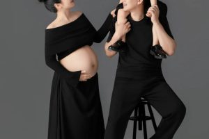 Ảnh chụp gia đình gồm bố, mẹ bầu và con trai trong trang phục màu đen trên nền studio xám.