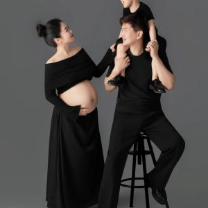 Ảnh chụp gia đình gồm bố, mẹ bầu và con trai trong trang phục màu đen trên nền studio xám.