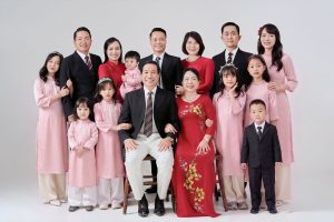 Ảnh chụp gia đình nhiều thế hệ mặc áo dài và vest trong studio với phông nền trắng.
