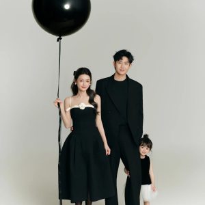 Ảnh chụp gia đình ba người với phong cách tối giản, sang trọng trong trang phục tông màu đen trên nền trắng.