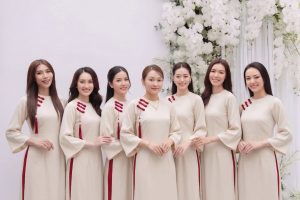 Nhóm các cô gái mặc áo dài trắng ngà phối đỏ thanh lịch trong studio với hoa trắng.