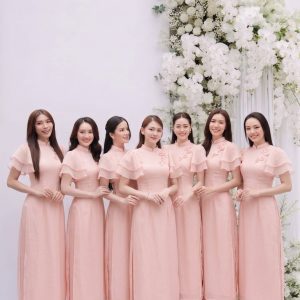 Nhóm các cô gái mặc áo dài hồng duyên dáng chụp tại studio với hoa trắng.