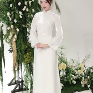 Cô dâu mặc áo dài trắng thanh lịch trong bối cảnh studio với hoa trắng.