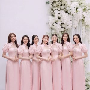 Một nhóm các cô gái mặc váy hồng pastel thanh lịch chụp tại studio với hoa trắng.