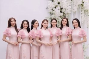 Nhóm các cô gái mặc áo dài hồng pastel chụp tại studio với hoa trắng.